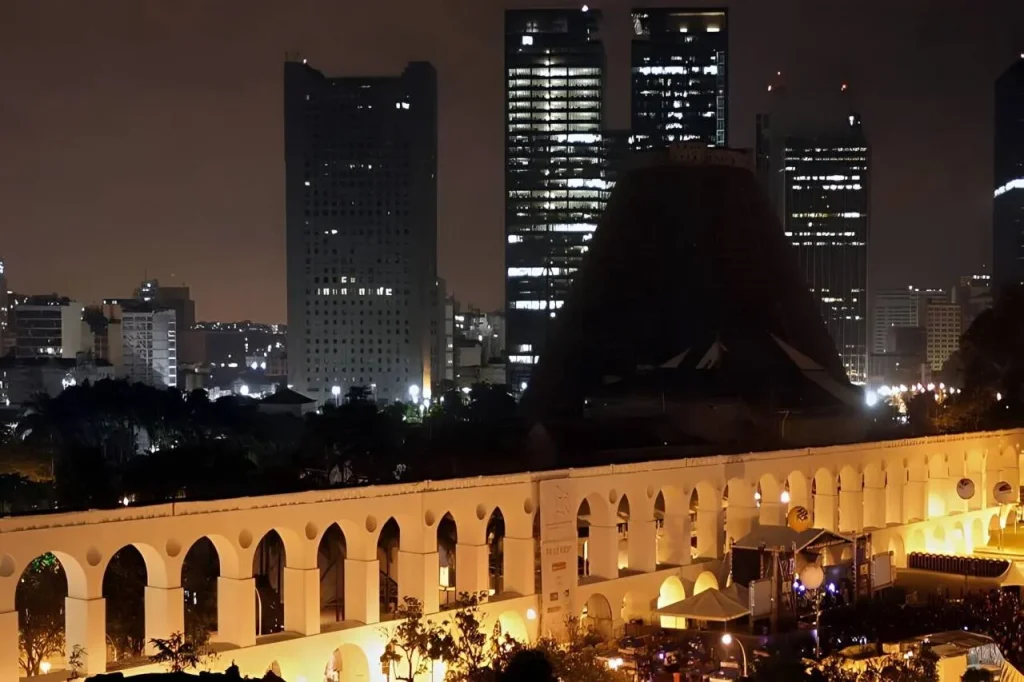 Movimentação noturna e mesas de bar sob os Arcos da Lapa iluminados.