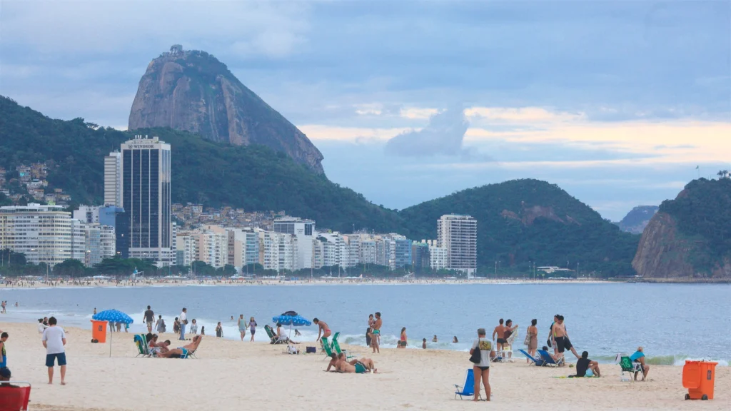 Pessoas diversas aproveitando o sol na areia da Praia de Copacabana perto de um posto de salvamento.